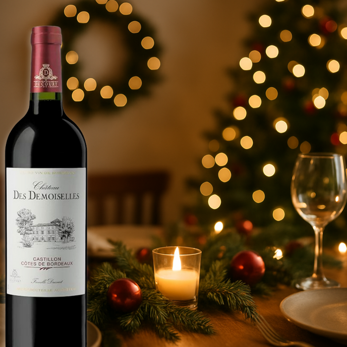 Bottle of Château Des Demoiselles wine on a table with Christmas decorations and lights.