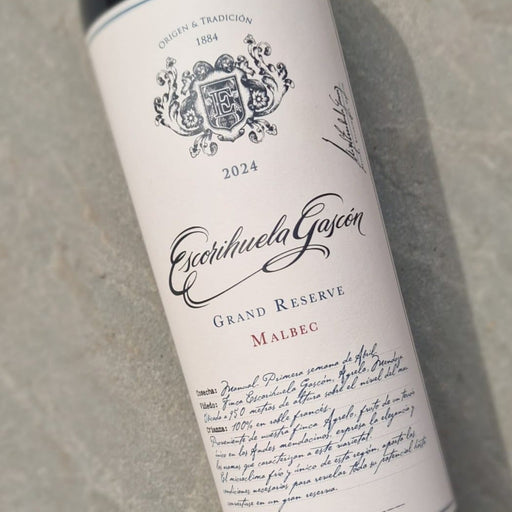 A bottle of Escribuela Garcia Malbec Grand Reserve wine resting on a textured gray concrete surface. The bottle has a dark glass body with a cream-colored label featuring elegant black script and crest details.