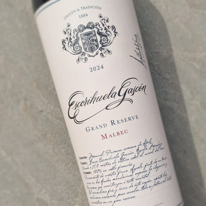 A bottle of Escribuela Garcia Malbec Grand Reserve wine resting on a textured gray concrete surface. The bottle has a dark glass body with a cream-colored label featuring elegant black script and crest details.
