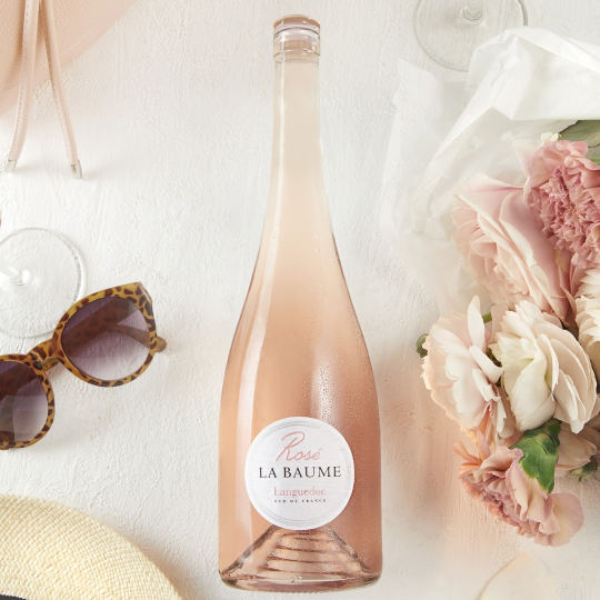 Bottle of La Baume Rosé champagne with sunglasses and flowers on a light background